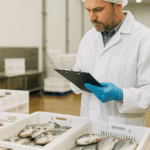 Curso de Implantación de Sistemas de Autocontrol APPCC en Productos de la Pesca: técnico de calidad revisando productos pesqueros en planta de procesamiento.